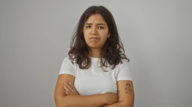 Esmer saçlı genç bir İspanyol kadın yüzünde ciddi bir ifadeyle duruyor, beyaz bir gömlek giyiyor, beyaz bir arka planda izole edilmiş..