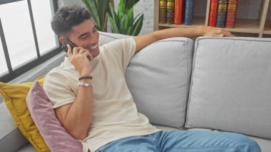 Yakışıklı İspanyol adam telefonda konuşurken gülümsüyor, evdeki kanepede dinleniyor..