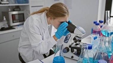 Laboratuvar ortamında deney tüpleri ve mataralarla mikroskop kullanan sarışın kadın bilim adamı..