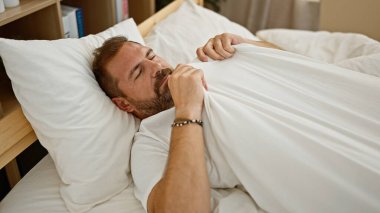 Gri saçlı olgun bir adam yatak odasında huzur içinde dinleniyor. Rahatlık ve aile huzuru simgeliyor..