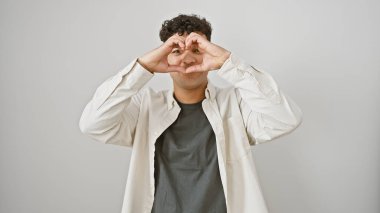Genç, Latin asıllı, kalbi şekillendiren genç bir adam beyaz, soyutlanmış bir arka plana karşı elleri ile pozitiflik ve şefkat gösteriyor..