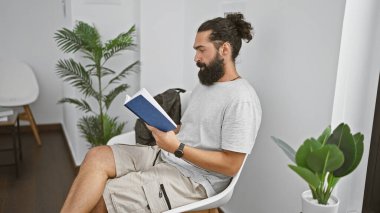 Modern bir salonda kitap okuyan sakallı yakışıklı İspanyol bir adam.