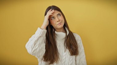 Beyaz kazaklı düşünceli genç İspanyol kadın sarı arka planda düşünceli bir şekilde poz veriyor..