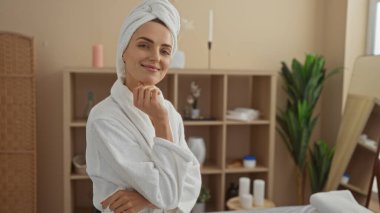 Kaplıca cüppeli güzel sarışın bir kadın, sakin ve sakin dekorlarla çevrili bir salonda kendine güvenerek gülümsüyor..