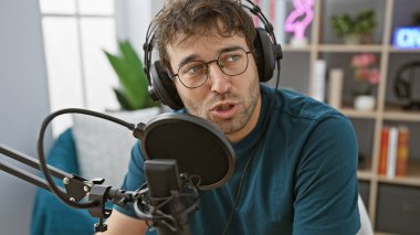 İçeride radyo stüdyosunda sakallı İspanyol adam mikrofona konuşuyor..