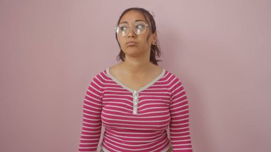 Çizgili tişörtlü genç bir İspanyol kadın pembe bir duvara karşı poz veriyor..