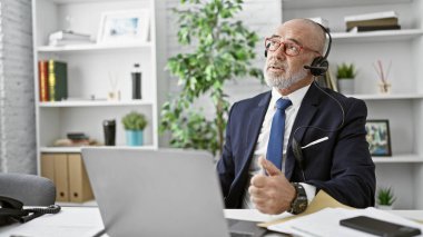 Kulaklığı olan profesyonel bir kıdemli modern ofis ortamında onaylar..