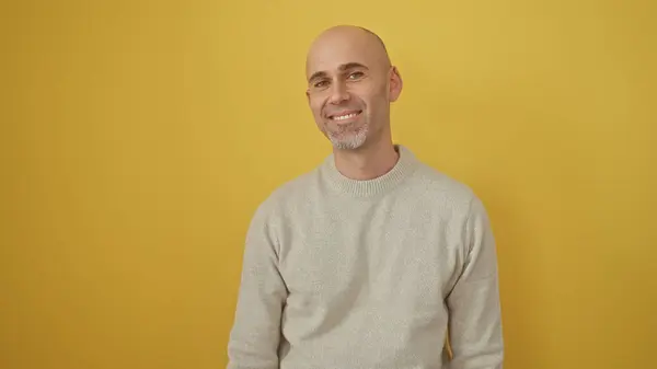 stock image A smiling bald man with a beard poses in a casual sweater against a vibrant yellow background, exuding friendly confidence.