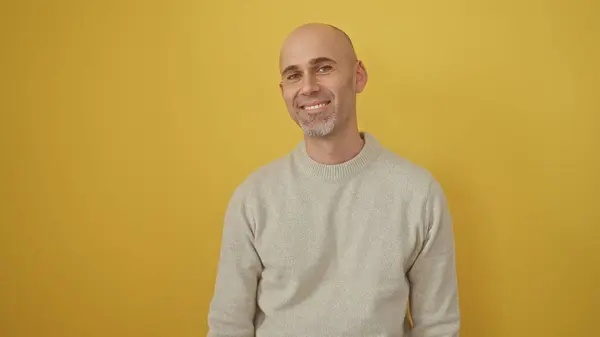 Stock image A smiling bald man with a beard poses in a casual sweater against a vibrant yellow background, exuding friendly confidence.