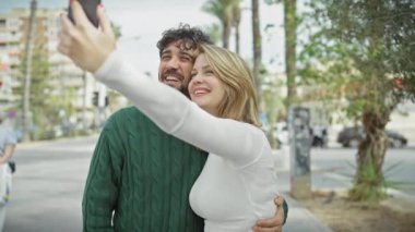 Mutlu çift şehir sokaklarında selfie çekiyor, bir erkek ve bir kadınla kucaklaşıyorlar ve dışarıda gülümsüyorlar..