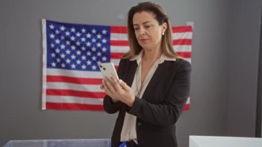 Bir iş kadını seçim sürecinin ortasında Amerikan bayrağına karşı seçim merkezinde telefonunu kontrol ediyor..