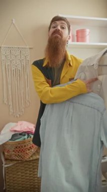 Sakallı bir adam tasarım odasında gömlekleri inceler, moda, zanaat, terzilik ve stil sahneleri yaratır..