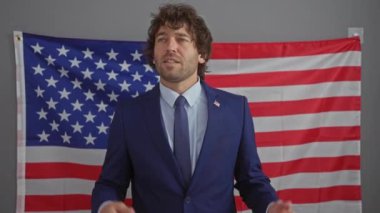 Takım elbiseli kendine güvenen genç bir adam Amerikan bayrağının önünde duruyor. İç mekanda vatansever bir ruhu somutlaştırıyor..
