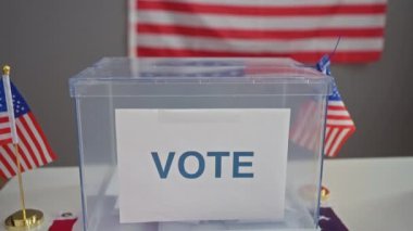 Amerika Birleşik Devletleri 'nde demokrasiyi ve seçimleri sembolize eden arka planda Amerikan bayrakları olan saydam bir oy sandığında oy kullanan bir kişi..
