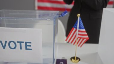 Amerikan bayrağı ve oy sandığıyla oy verme merkezinde akıllı telefon kullanan Afrikalı Amerikalı bir kadın..