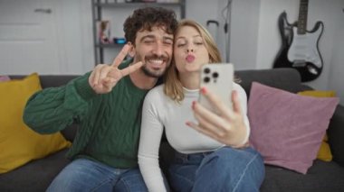 Neşeli bir adam ve kadın modern dekorlu rahat bir oturma odasında selfie çekerken birlikte vakit geçiriyorlar..