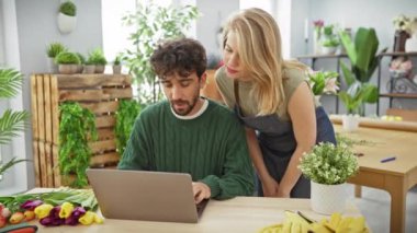 Erkek ve kadın canlı laleler ve yeşillikler arasında dizüstü bilgisayar kullanarak bir çiçekçide iş birliği yapıyorlar..