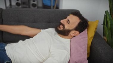 Yakışıklı, orta yaşlı bir adam, evinde neşeyle gülümsüyor, gözleri eğlence amaçlı kör oyunlarda kollarla kaplanıyor. Beyaz tişörtlü, neşeli ifadesi karşı konulmaz derecede komik. Mükemmel ev sürprizi.!