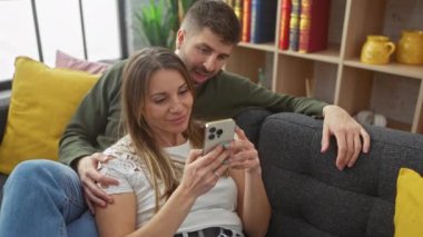 Sevgi dolu bir çift, rahat bir oturma odasında akıllı telefon kullanarak birlikte vakit geçirmekten zevk alır.