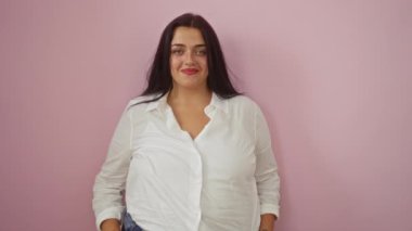 Pembe arka planda, beyaz gömlek giyen ve neşeli bir tavır sergileyen genç bir kadın.