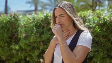 Sarışın, genç, kadın şehir parkında alerjisi olan güneşli bir günde yeşil yaprakların yanında duran..