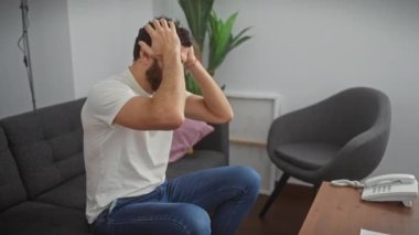 Stresli orta yaşlı bir adam, ağrıyan kafasını elinde tutuyor, beyaz bir tişört giyerken şiddetli migren ağrısı ve stresle mücadele ediyor.