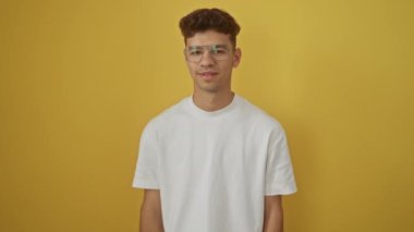 Beyaz tişörtlü, mutlu, genç İspanyol bir adam olumlu gülümseyen, onay işareti veren ve izole edilmiş sarı arka planda mükemmel bir jest yapan.