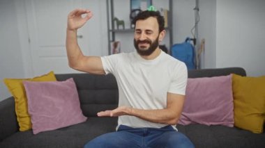 Neşeli orta yaşlı adam evinde kocaman bir tabela gösteriyor. Beyaz tişörtü ile 