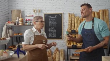 Kadın ve erkek fırıncılar ekmek ve hamur işleriyle çevrili fırının içinde tartışıyor raflarda ve tezgahlarda
