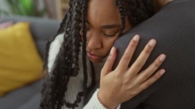 Bir kadın, rahat bir oturma odasında bir erkeği kucaklar. Huzurlu bir evde aşkı ve arkadaşlığı sembolize eder..