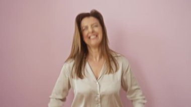 Neşeli bir gülümseme ve kazanan bir ifadeyle zaferi kutlayan İspanyol bir kadın pembe izole edilmiş arka planda dikilirken gömlek giyiyor.