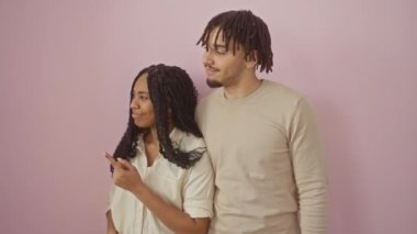 Güzel bir çift, hepsi gülümsüyor, güvenle duruyorlar ve kenarları işaret ediyorlar, izole edilmiş pembe bir arka plana neşe saçıyorlar.