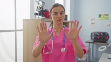 Pembe önlüklü genç bir kadın doktor ellerini kapalı bir klinikte ya da hastane ortamında durdurur..