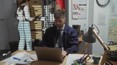 Odaklanmış bir erkek ve kadın, karmaşık bir polis merkezinde özenle çalışarak soruşturmanın özenli doğasını somutlaştırıyor..