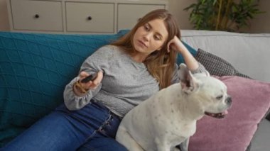 Oturma odasındaki rahat bir kanepede köpeğiyle rahat bir anın tadını çıkaran genç bir kadın rahat dairesinde televizyon izliyor..
