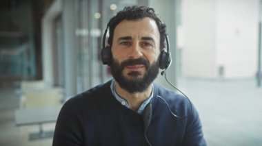 Ofisteki sakallı bir adam, kulaklık takıyor, içten gülümsüyor, profesyonelliği ve yakınlığı somutlaştırıyor..