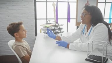 Beyaz önlüklü bir kadın doktor, klinikte gülümseyen bir çocuğu muayene ediyor..