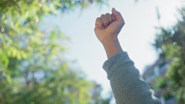 Parkta bir adamın yumruğu, gücü simgeliyor ve açık bir gökyüzü altında, yeşilliklerle gizlenmiş bir şekilde protesto ediyor..