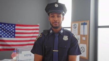 Üniformalı, gülümseyen Afro-Amerikan polisi oy kullanma merkezindeki kamerayı işaret ediyor.