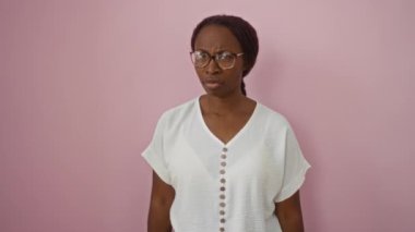 Genç Afro-Amerikalı kadın, gözlük takıyor, ayakta duruyor ve somurtuyor, bir soruna üzülüyor, sinirli şüpheci, pembe bir arka planda izole edilmiş negatif bir ifadeyle.