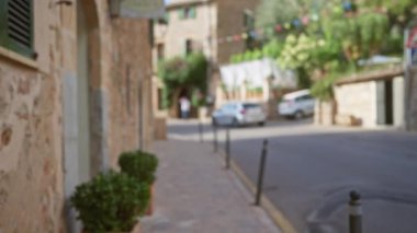 Mallorca, İspanya 'daki bulanık hava manzarası arka planda dağılmış arabaları ve binaları taştan bir patika boyunca yürüyen bulanık yayaları gösteriyor.