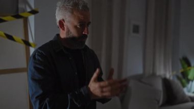 Hafif ışıklandırılmış ev ortamında kelepçeli sıkıntılı bir adam olay yeri incelemesini ima ediyor..