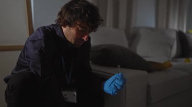 Araştırmacı bir adam, kapalı bir suç mahalli düzeneğine odaklanarak delilleri inceler ve bir miktar belirsizlik ekler..