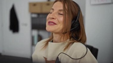 Genç, çekici sarışın kadın, kulaklık takıyor, gülümsüyor ve modern bir ofis içine bakıyor..