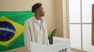 Genç, yakışıklı, Afro-Amerikalı bir erkek, kapalı bir üniversite odasında Brezilya bayrağıyla oy kullanıyor..