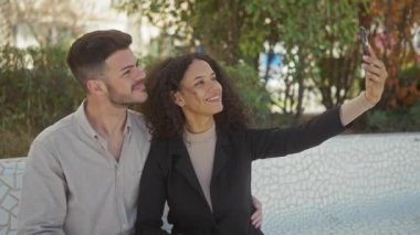 Gülümseyen kadın ve erkek güneşli bir parkta selfie çekiyorlar.