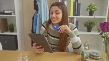 Kredi kartıyla gülümseyen İspanyol kadın evde online alışveriş için tablet kullanıyor..