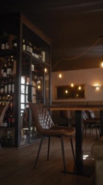 Loş ışıklandırma, şarap şişeleri ve şık mobilyalarla dolu boş bir modern restoran iç mekanı samimi bir yemek atmosferini çağrıştırıyor..
