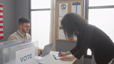 Bir erkek ve bir kadın kapalı bir Amerikan sandık merkezinde Amerikan bayrağıyla etkileşime geçiyorlar.