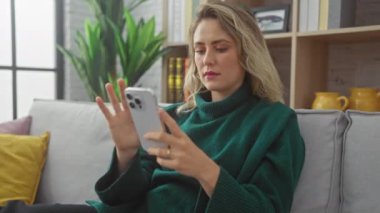 Beyaz kadın rahat oturma odasının iç tarafındaki kanepede akıllı telefon kullanıyor.